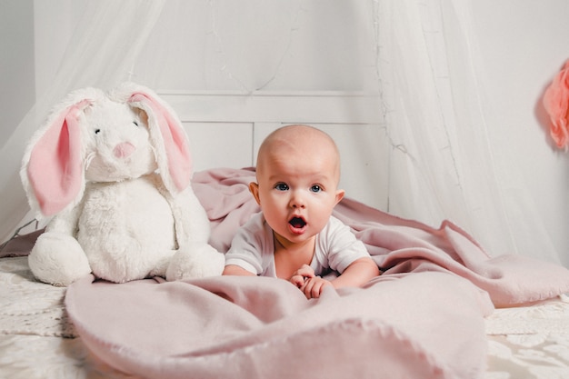 Un pequeño bebé se acuesta en la cama con un conejo de juguete y sonríe.