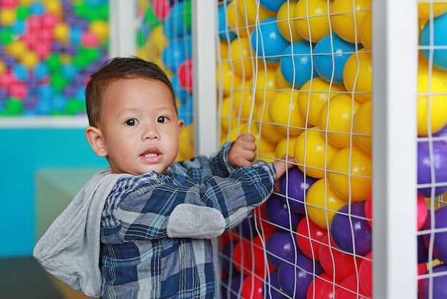 Pequeño bebé adorable que juega la bola plástica colorida en jaula con la mirada de la cámara.