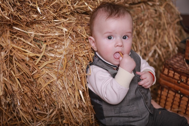 El pequeño bebé adorable se sienta cerca de los pajar en el interior y mira a los ojos serios.