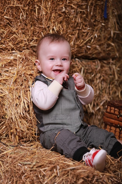 El pequeño bebé adorable se sienta cerca de los pajar en el interior y mira a los ojos serios.