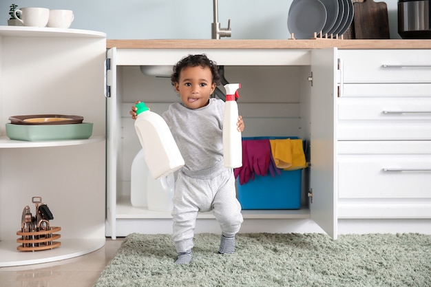 Pequeño bebé afroamericano jugando con detergentes en casa. Niño en peligro