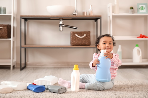 Foto pequeño bebé afroamericano jugando con líquidos de lavado en casa. niño en peligro