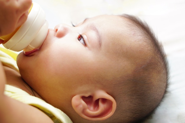 Un pequeño bebé asiático bebiendo leche del biberón en la cama el concepto de empatía adorable y bonito