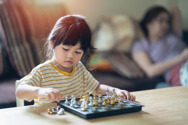 Pequeño bebé asiático jugando al ajedrez en la sala de estar en casaNiños inteligentes de moda para niños Pequeño genio Juego inteligente para niños Tablero de ajedrez Concepto de actividad para bebés