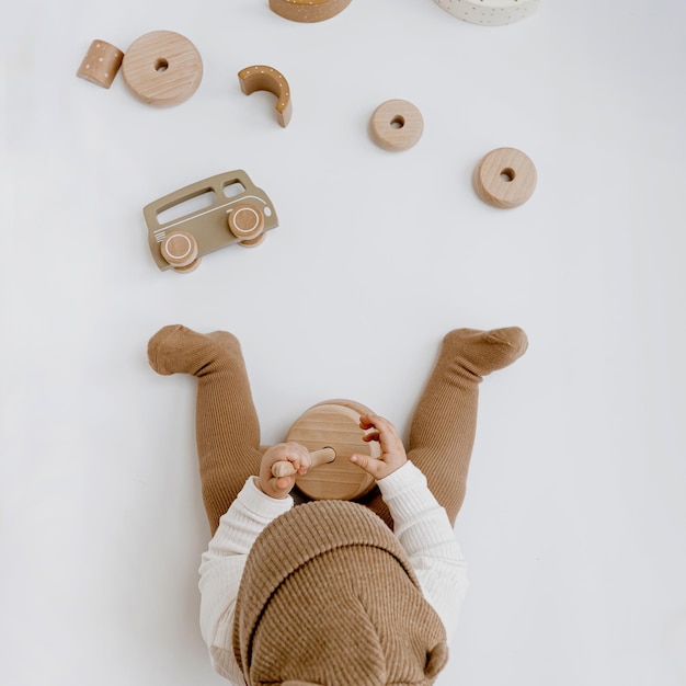 Pequeno bebê com roupas elegantes brinca com brinquedos de madeira moda roupas e brinquedo de recém-nascido escandinavo vista superior plana