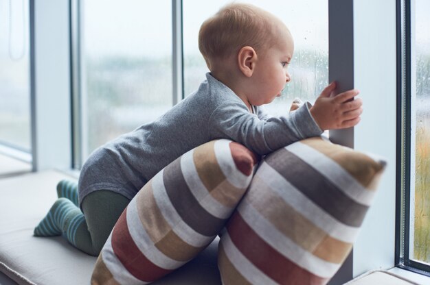 Pequeño bebé crawlibg cerca de la ventana grande en las almohadas.