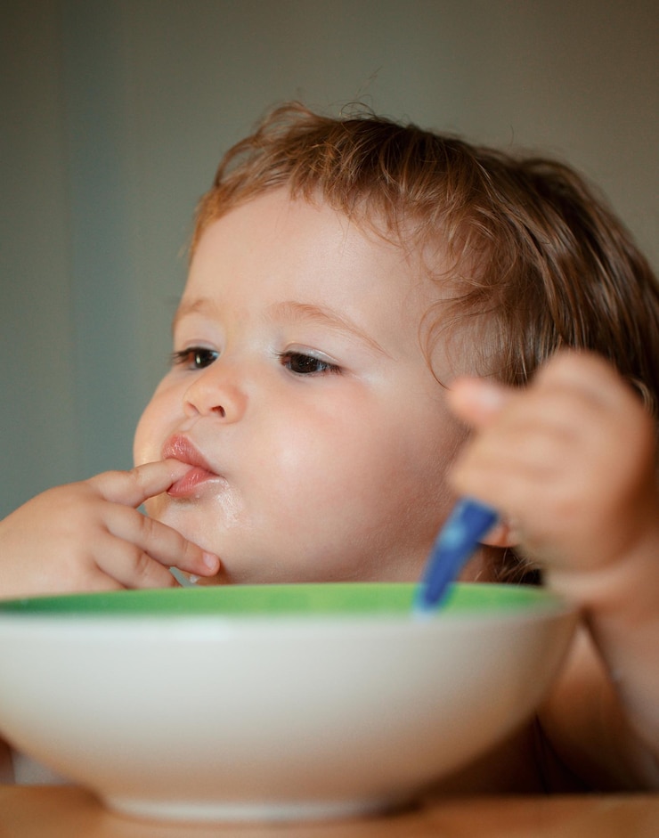 Foto pequeño bebé divertido en la cocina comiendo con los dedos del plato lamer los dedos sabrosos