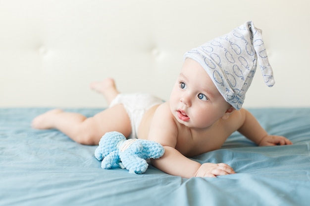 Pequeño bebé divertido con grandes ojos azules sonriendo con linda gorra en la cabeza