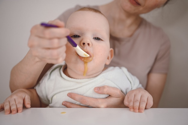 Pequeño bebé divertido recién nacido aprendiendo a comer puré de frutas o verduras de un frasco de vidrio con una cuchara
