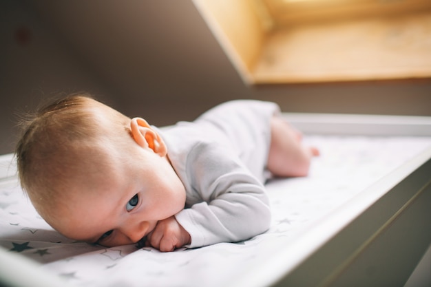 Pequeño bebé está acostado en la mesa de los niños junto a la ventana. Hay un niño recién nacido en la mesa para cambiar pañales.