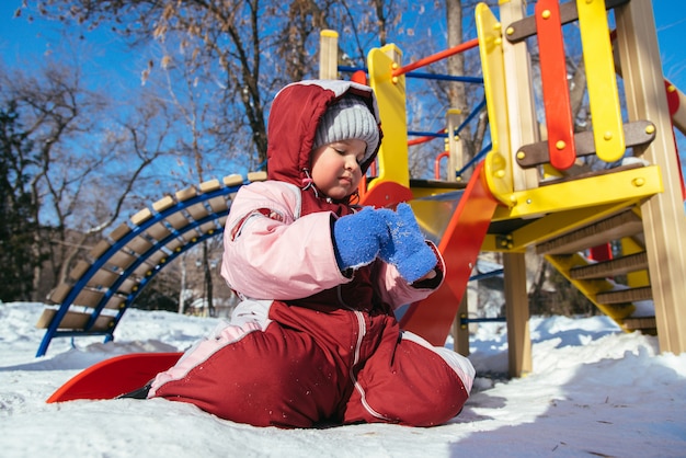 Pequeño bebé juega en el patio de recreo en invierno