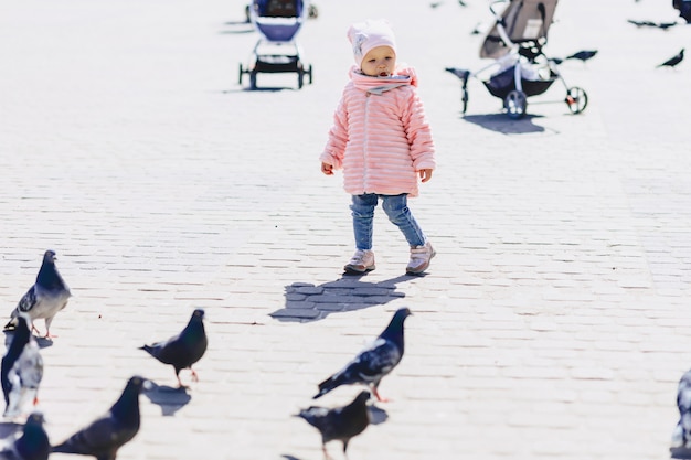 Pequeño bebé lindo caminar en la plaza con aves