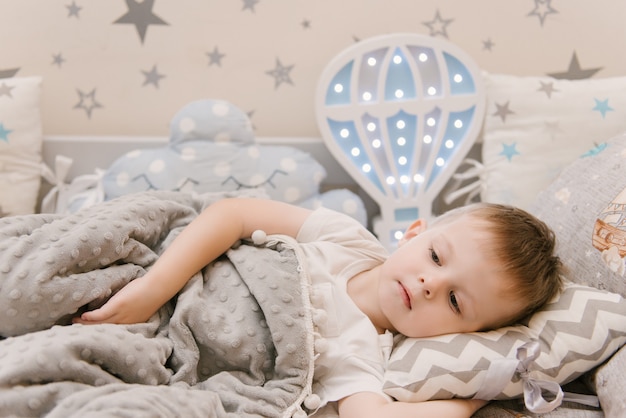 Pequeño bebé lindo se encuentra en la habitación de los niños en una casa de cama de madera con luces nocturnas en forma de globo, el bebé se duerme en la cuna