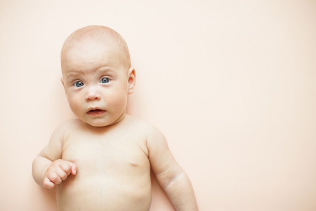 El pequeño bebé lindo miente en un fondo rosa claro.