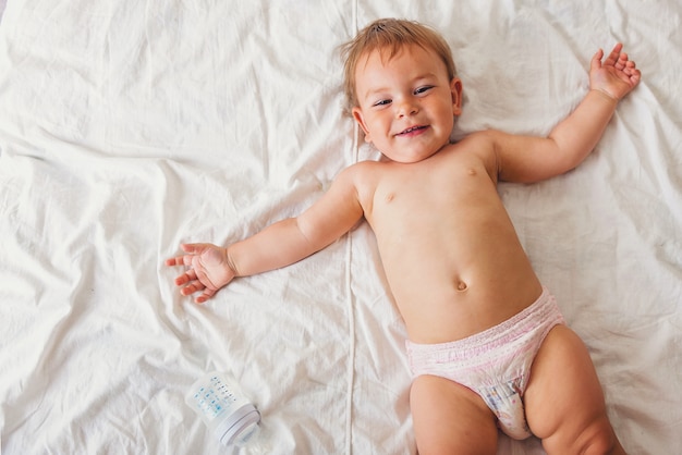 Pequeño bebé lindo que miente en la cama blanca y que sonríe feliz, niñez