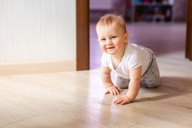 Pequeño bebé lindo que miente en la madera dura y la sonrisa. Niño gateando sobre parquet de madera.