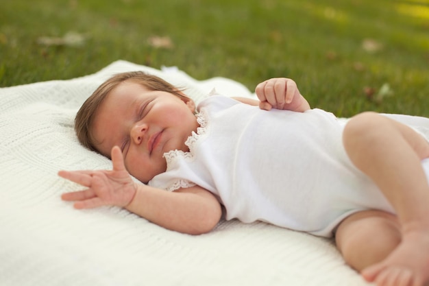 Pequeño bebé lindo con ropa blanca durmiendo en la sábana blanca sobre la hierba