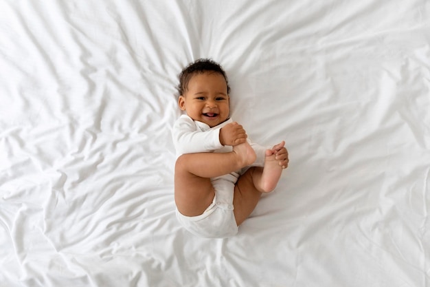 Pequeño bebé negro divertido que se divierte mientras está acostado en la cama en casa