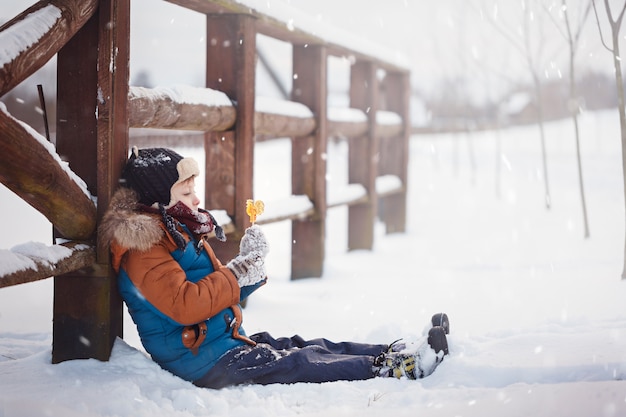Foto pequeño bebé que juega y que come el gallo dulce en día de invierno. los niños juegan en el bosque nevado.