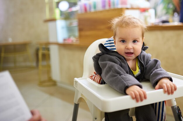 Pequeño bebé sentado en una silla alta en la cafetería