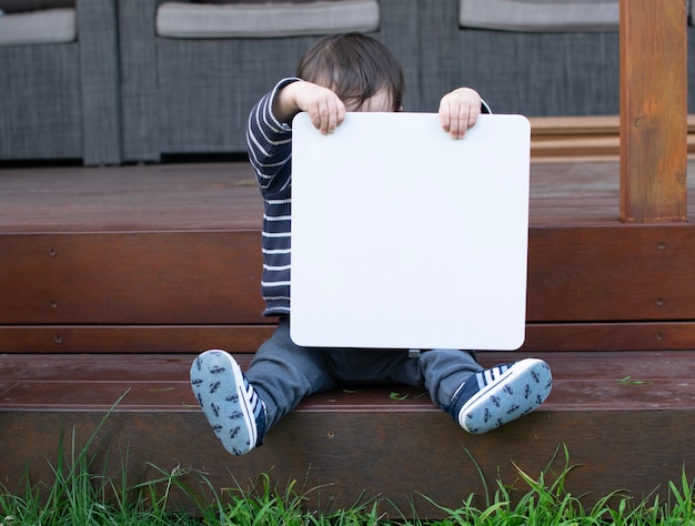 Pequeño bebé sentarse y sostener el tablero blanco