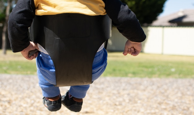 El pequeño bebé se sienta en el asiento elástico del columpio, relaja los brazos y las piernas.