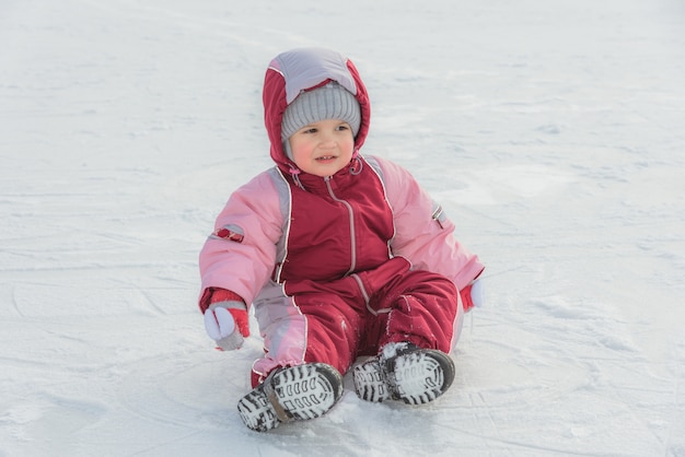 Pequeño bebé se sienta en el hielo en invierno