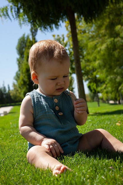 Foto un pequeño bebé se sienta en la hierba del parque y estudia las briznas de hierba juega con la hierbaverano y el sol brillanteun paseo al aire libre