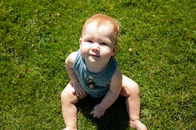 El pequeño bebé se sienta en la hierba del parque y sonríeVerano y sol brillantePaseo al aire libre