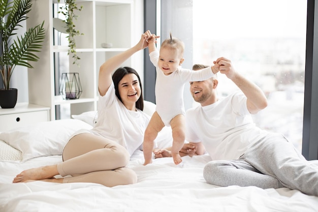 Pequeño bebé sonriente dando los primeros pasos en la cama con sus padres