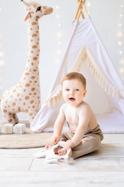 Un pequeño bebé sonriente jugando en la guardería, una luminosa y acogedora habitación para niños, textiles naturales y juguetes de madera para la guardería.