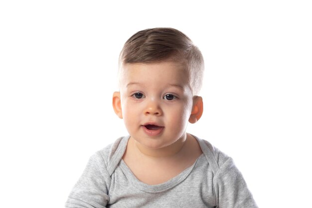 Pequeño bebé sonriente en mono sentado descalzo en el suelo aislado en blanco