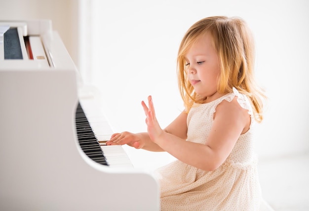 Un pequeño bebé toca un gran piano blanco en una habitación luminosa y soleada