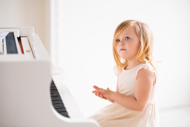 Un pequeño bebé toca un gran piano blanco en una habitación luminosa y soleada