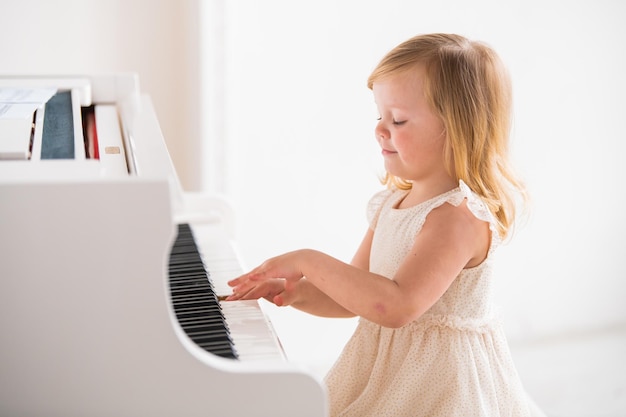 Un pequeño bebé toca un gran piano blanco en una habitación luminosa y soleada