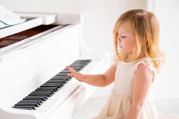 Un pequeño bebé toca un gran piano blanco en una habitación luminosa y soleada