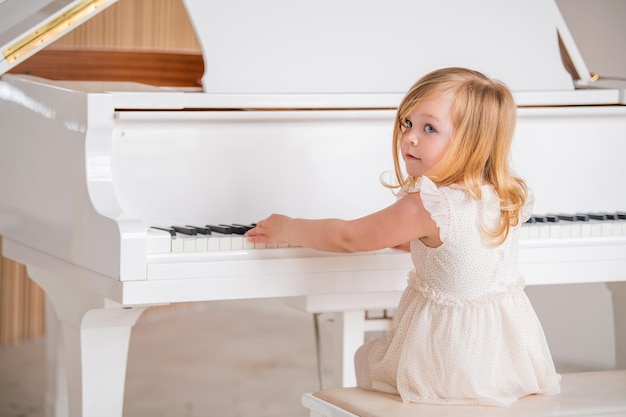 Un pequeño bebé toca un gran piano blanco en una habitación luminosa y soleada