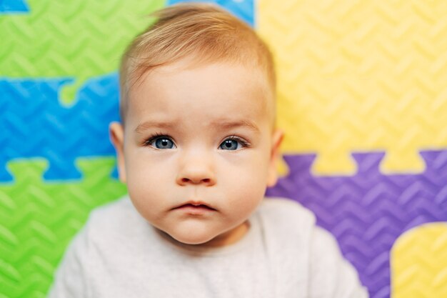 Pequeño bebé en un traje blanco está acostado sobre una alfombra de color closeup retrato