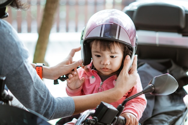 El pequeño bebé usa un casco de motocicleta cuando su madre lo sujeta en la motocicleta