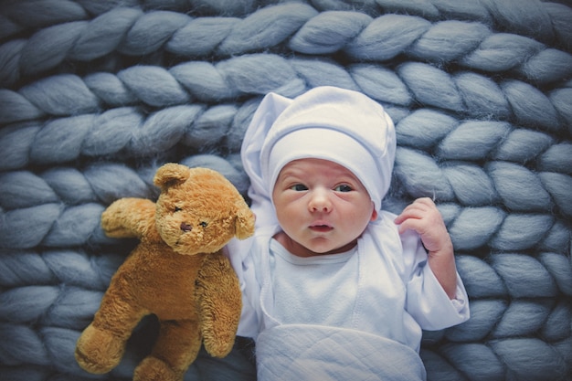 pequeño bebé vestido con una ropa blanca y un sombrero con oso taddy