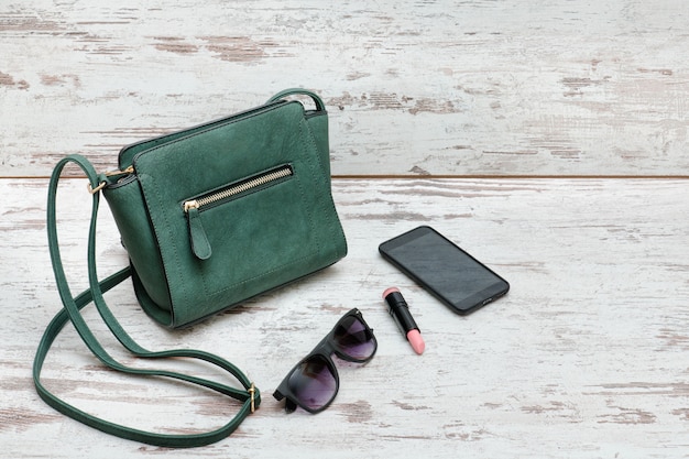 Pequeño bolso verde, gafas de sol, lápiz labial y teléfono inteligente