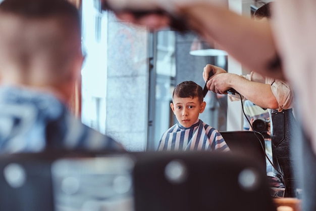 El pequeño y bonito colegial tuvo su primer corte de pelo a la moda en la barbería moderna.