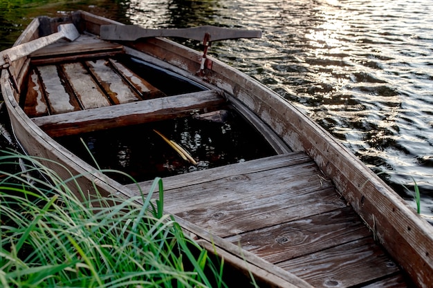 Un pequeño bote de remos de madera con un fondo roto en un lago tranquilo cerca de la orilla.