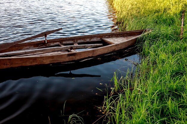 Un pequeño bote de remos de madera con un fondo roto en un lago tranquilo cerca de la orilla.