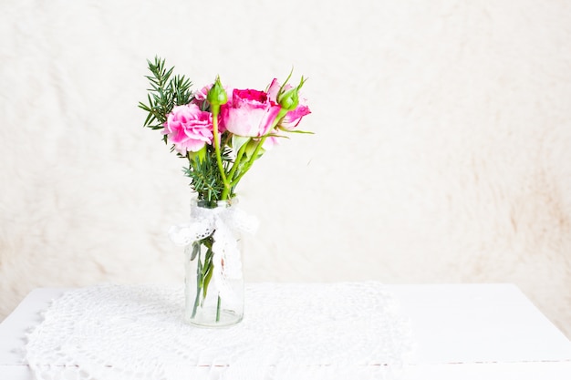 Pequeno bouquet aconchegante em frasco de vidro sobre guardanapo de crochê. Estilo vintage