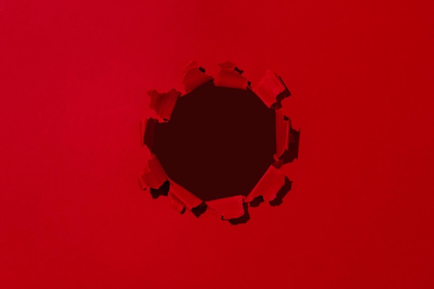 Pequeno buraco no espaço vazio de papel vermelho para texto publicitário em textura de fundo de papel rasgado