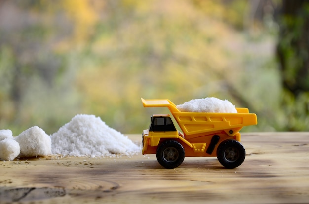 Un pequeño camión de juguete amarillo está cargado con una piedra de sal blanca junto a un montón de sal.