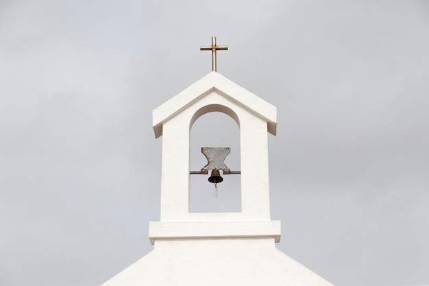 Pequeño campanario con campana y cruz, de iglesia rural.