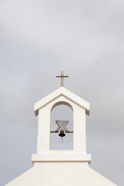 Pequeño campanario con campana y cruz, de iglesia rural.