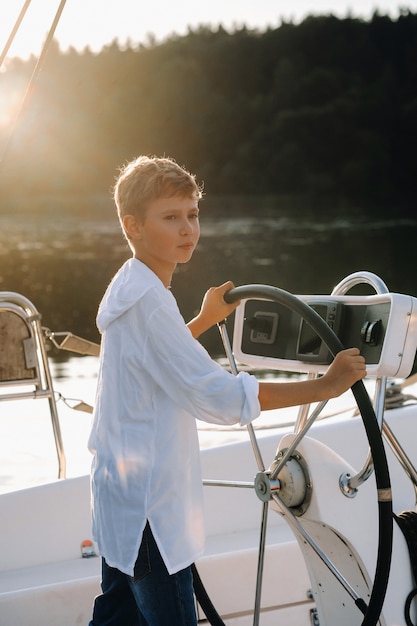 Un pequeño capitán al timón de un yate. un niño al timón del capitán en un yate al atardecer.